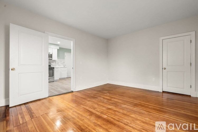 A room with wooden floors and white walls, with a door on the left and another on the right.