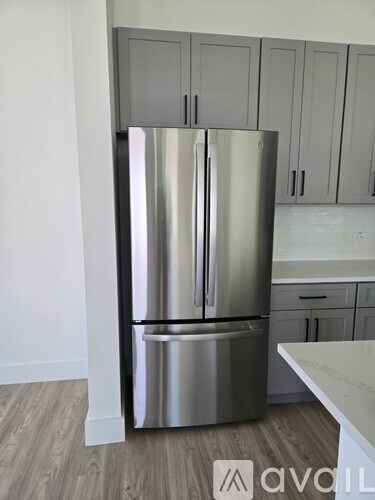 A stainless steel refrigerator in a kitchen with wooden floors and white cabinets.