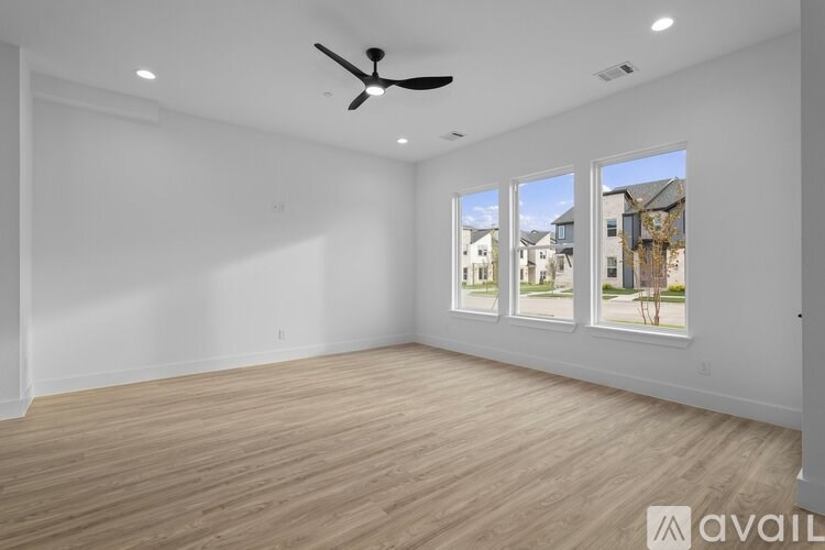 A spacious room with a ceiling fan and large windows overlooking a residential area.