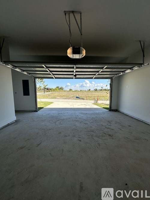 A large empty garage with a door open to a field.