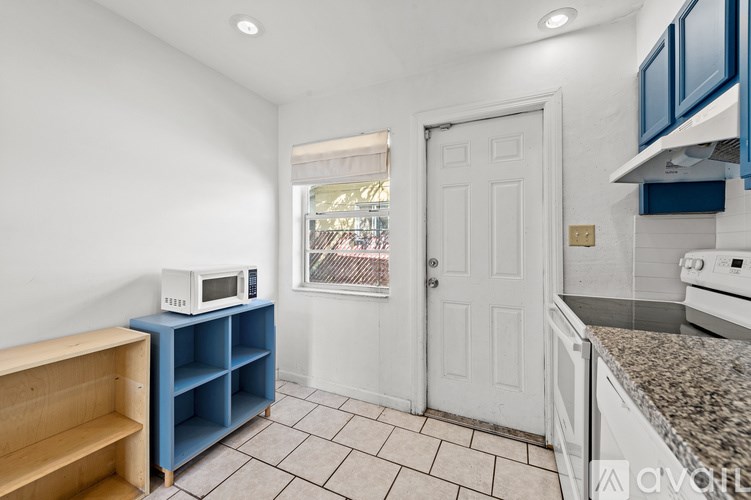 A kitchen with a white door and a microwave on a blue shelf.