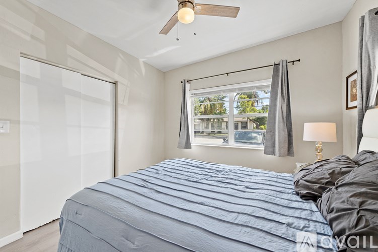 A bedroom with a bed, a ceiling fan, and a window with curtains.