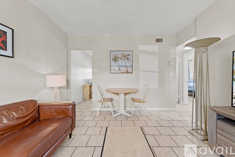 A living room with a brown leather couch, a white table, and a painting of a palm tree on the wall.