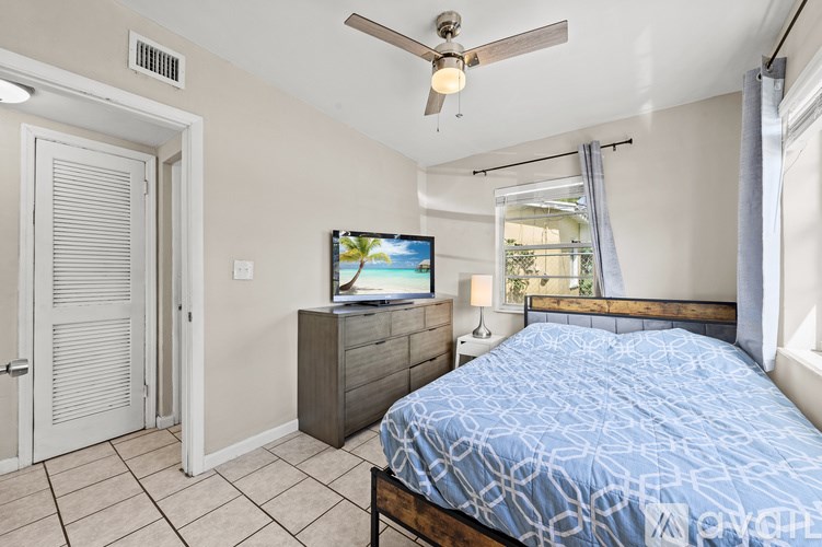 A bedroom with a bed, a television, and a ceiling fan.