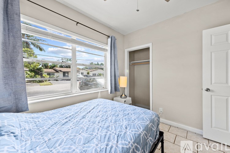A bedroom with a bed, a window with a view of the street, and a lamp on a side table.