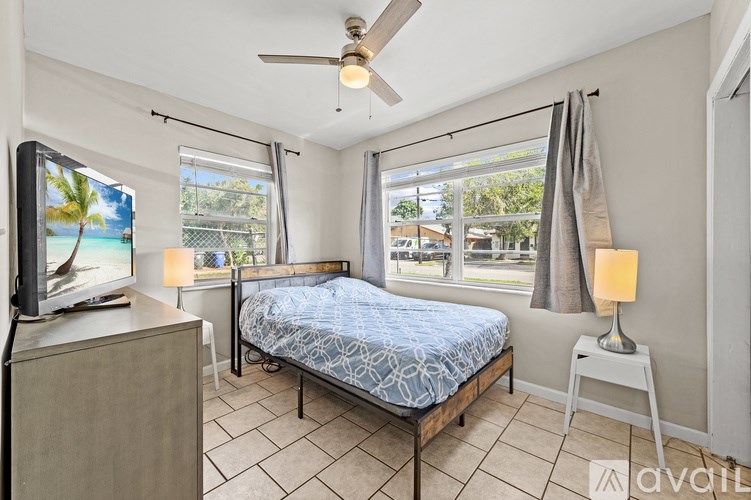A bedroom with a bed, a television, and a ceiling fan.