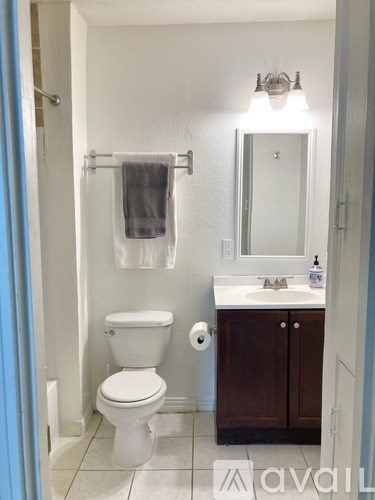 A white toilet is in a bathroom with a white sink and brown cabinets.