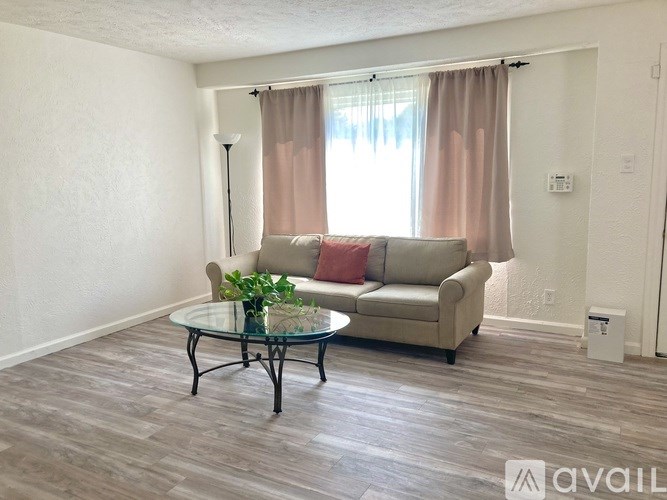 A living room with a couch, coffee table, and window with curtains.