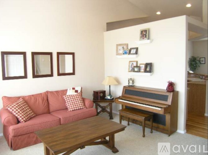 A living room with a pink couch, a wooden coffee table, a piano, and pictures on the wall.