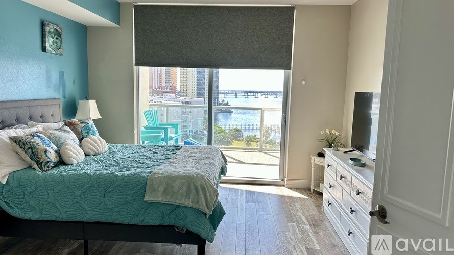 A bedroom with a bed, dresser, and a window overlooking a cityscape.
