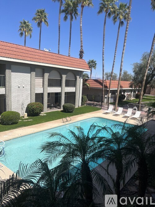 A pool surrounded by palm trees and a building with a red roof.