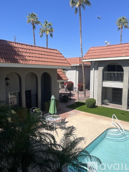 A pool surrounded by palm trees and a building with a red tile roof.