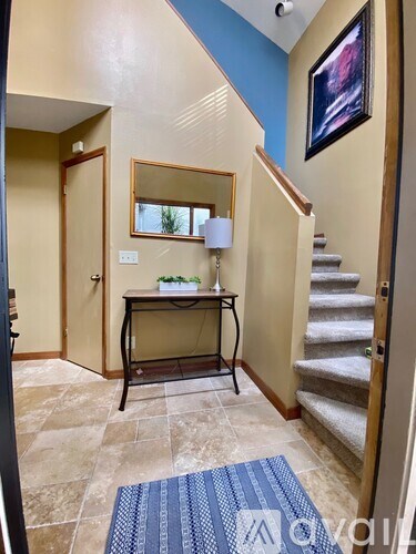 A hallway with a staircase, a mirror, a console table, and a rug.