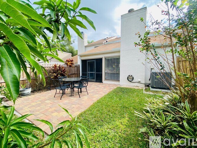 A patio with a table and chairs is surrounded by green plants.