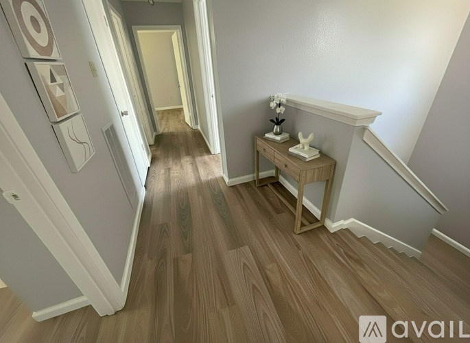 A hallway with a wooden floor and a white wall with a framed picture of a target on it.