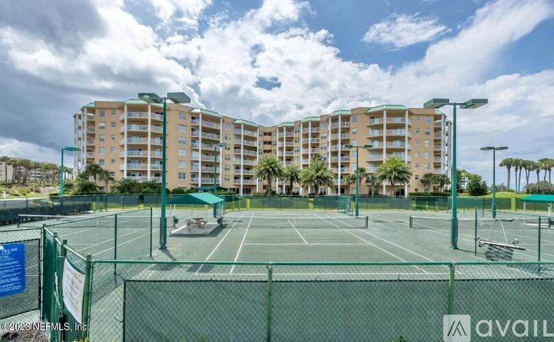 A tennis court is surrounded by a green fence and apartment buildings.