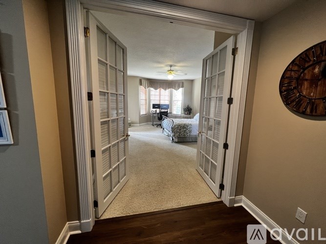 A hallway with a carpeted floor, a ceiling fan, and a wall clock.