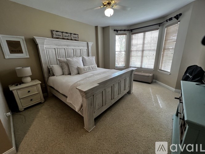 A bedroom with a large bed, a nightstand, and a window with blinds.