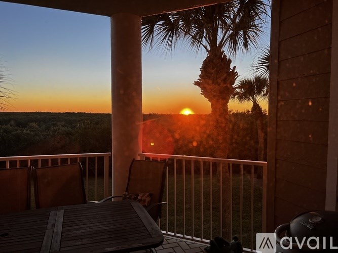 A balcony with a table and chairs overlooks a sunset.