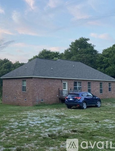 A car is parked in front of a brick building with a grassy field in the foreground.