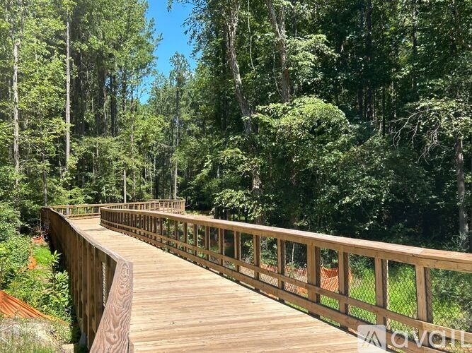 A wooden bridge in a forest with a railing on the right side.