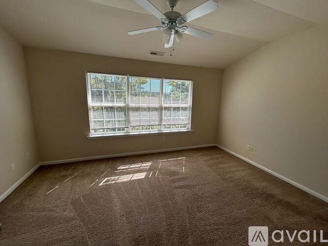 A room with a carpeted floor, a ceiling fan, and a window with blinds.