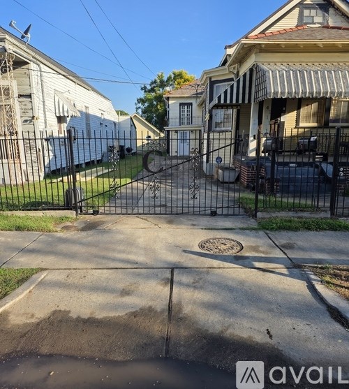 A residential street with houses on either side and a metal fence in the foreground.