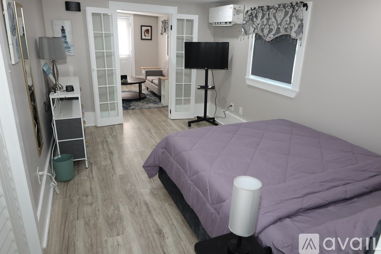 A bedroom with a purple bedspread and a television in the corner.