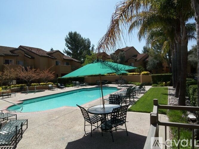 A pool with chairs and an umbrella in the foreground with houses in the background.