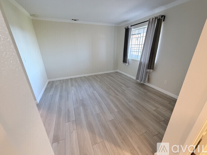 A room with wooden flooring and a window with curtains.