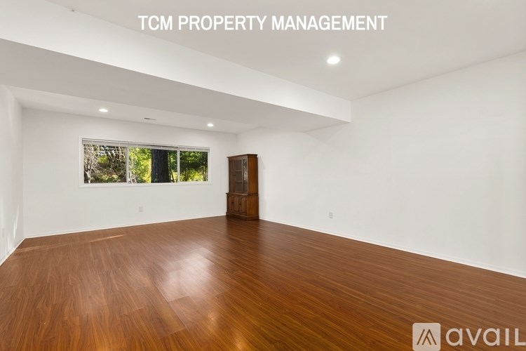 A spacious room with wooden flooring and a window overlooking greenery.