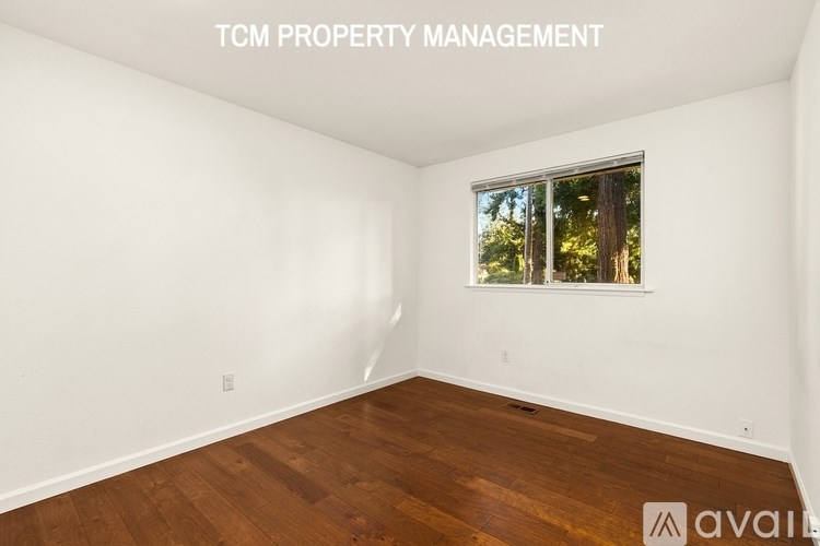 A room with wooden flooring and a window showing trees outside.