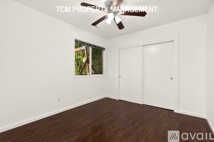A room with a ceiling fan and a window showing greenery outside.