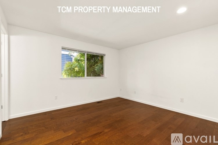 A room with wooden flooring and a window showing greenery outside.