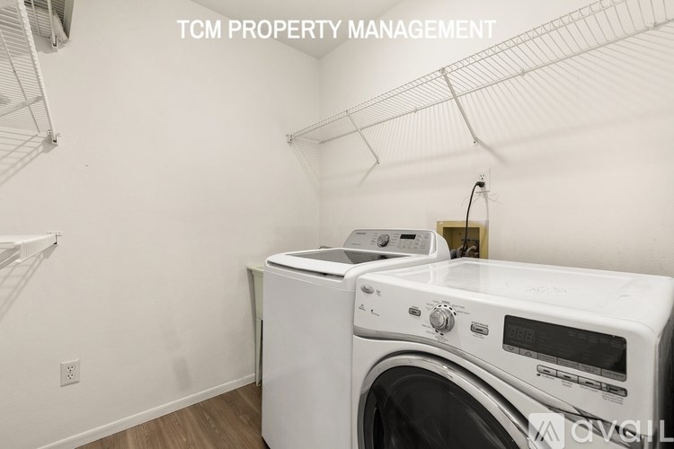 A white washing machine in a laundry room with the text "TCM PROPERTY MANAGEMENT" on the wall.