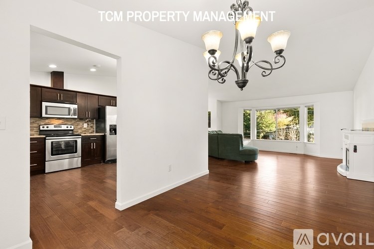 A well-lit, spacious kitchen and living room with wooden floors and a chandelier.