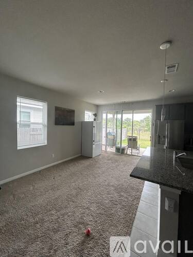 A room with a carpeted floor and a kitchen area with a sink and refrigerator.