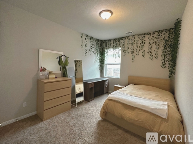 A bedroom with a bed, dresser, and window with greenery.