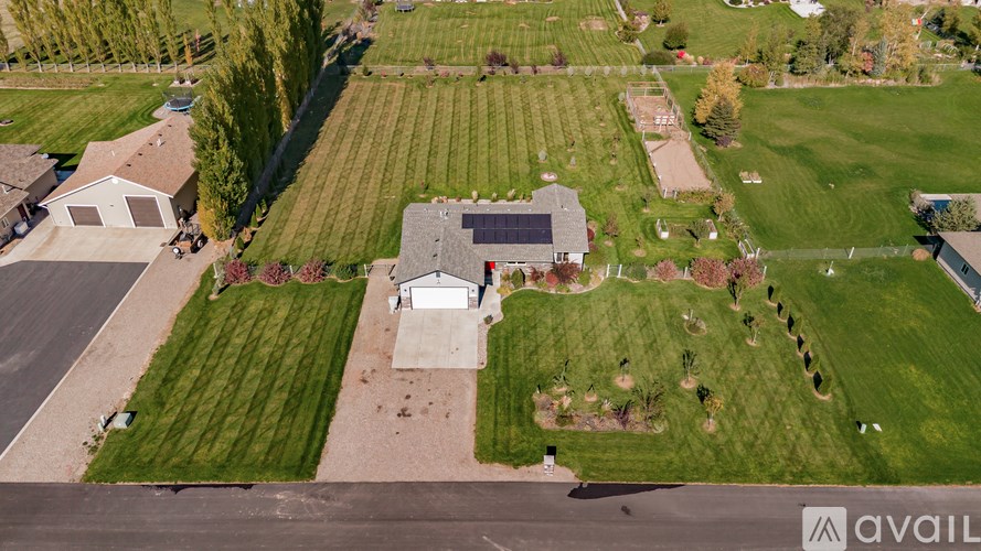 A large house with a grey roof is surrounded by a green lawn and a large field.