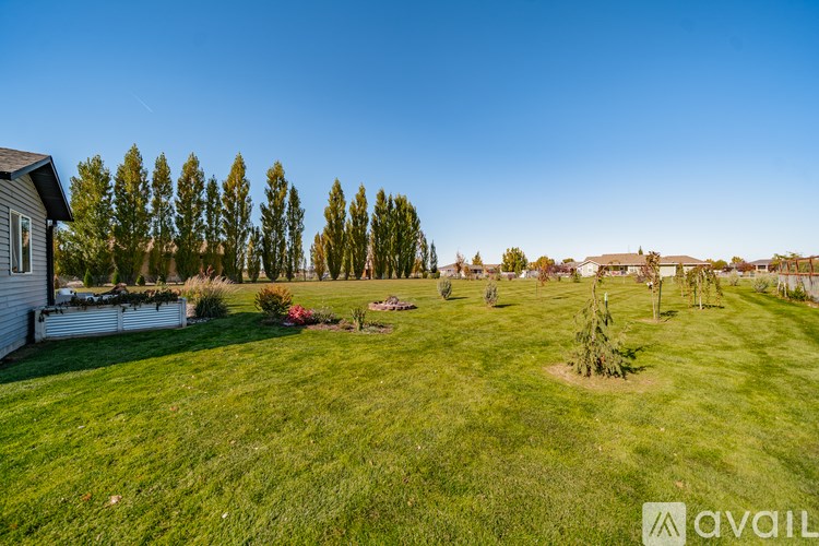 A grassy field with a house and trees in the background.