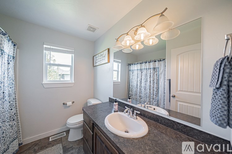 A bathroom with a sink, mirror, toilet, and a window.
