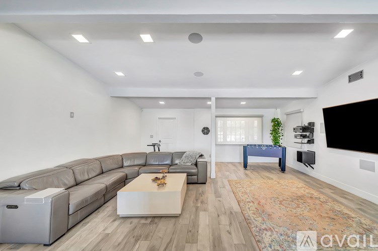 A modern living room with a grey sofa, a white coffee table, and a large flat-screen TV mounted on the wall.