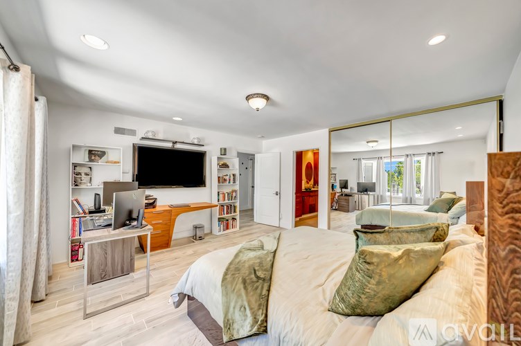 A bedroom with a bed, a desk with a laptop, and a bookshelf with books.