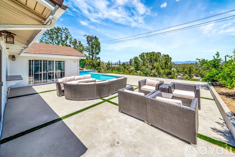A patio with a couch and a table is surrounded by a pool and a house.