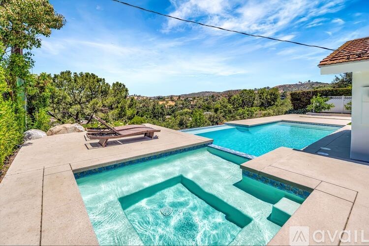 A large outdoor swimming pool surrounded by a concrete patio and a white house.