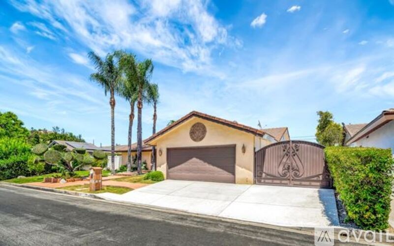 A house with a brown garage door is surrounded by greenery and other houses.