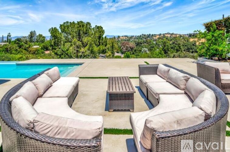 A patio with a pool and furniture is surrounded by trees.