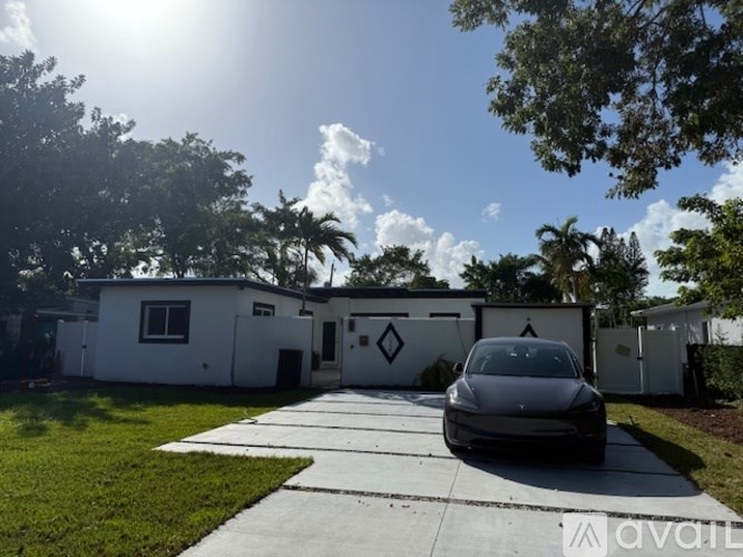 A car is parked in front of a white building with a driveway leading to the entrance.