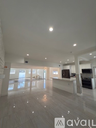 A spacious, well-lit living room with a kitchen area in the background.
