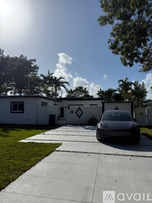 A car is parked in front of a white building with a tree on the left side.